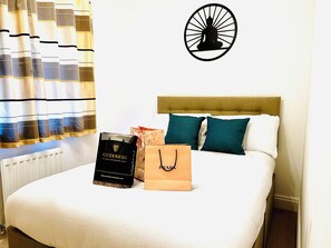Una habitación de hotel con cama, cabecera, decoración en la pared y una ventana con cortinas.