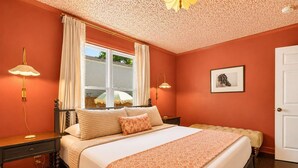 Una camera da letto con un letto, due comodini, una finestra con tende, un quadro appeso al muro e una porta.