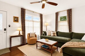 Ein Wohnzimmer mit Sofa, Sessel, Couchtisch und Deckenventilator.