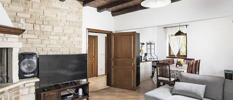 A living room with a stone fireplace, a flat-screen TV, a sofa, and a dining area with a table and chairs.