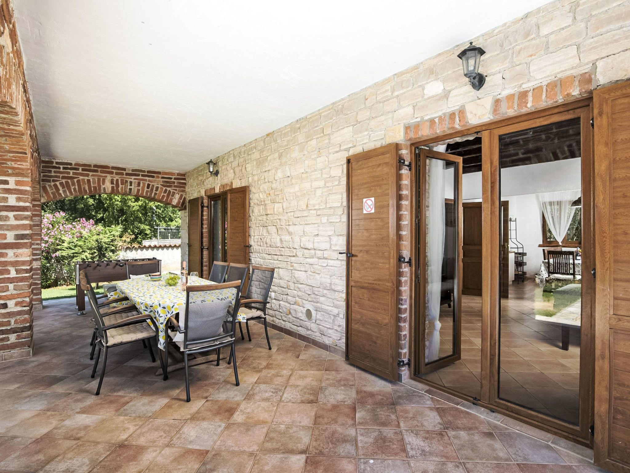 A covered patio with a brick wall, a table with chairs, and a sliding glass door leading to an interior space.