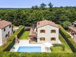 Una casa de pedra de dos pisos amb una piscina, envoltada d'un jardí ben cuidat i una zona boscosa.