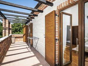 Un balcón con una pérgola de madera, un tendedero de metal y un muro de ladrillo.