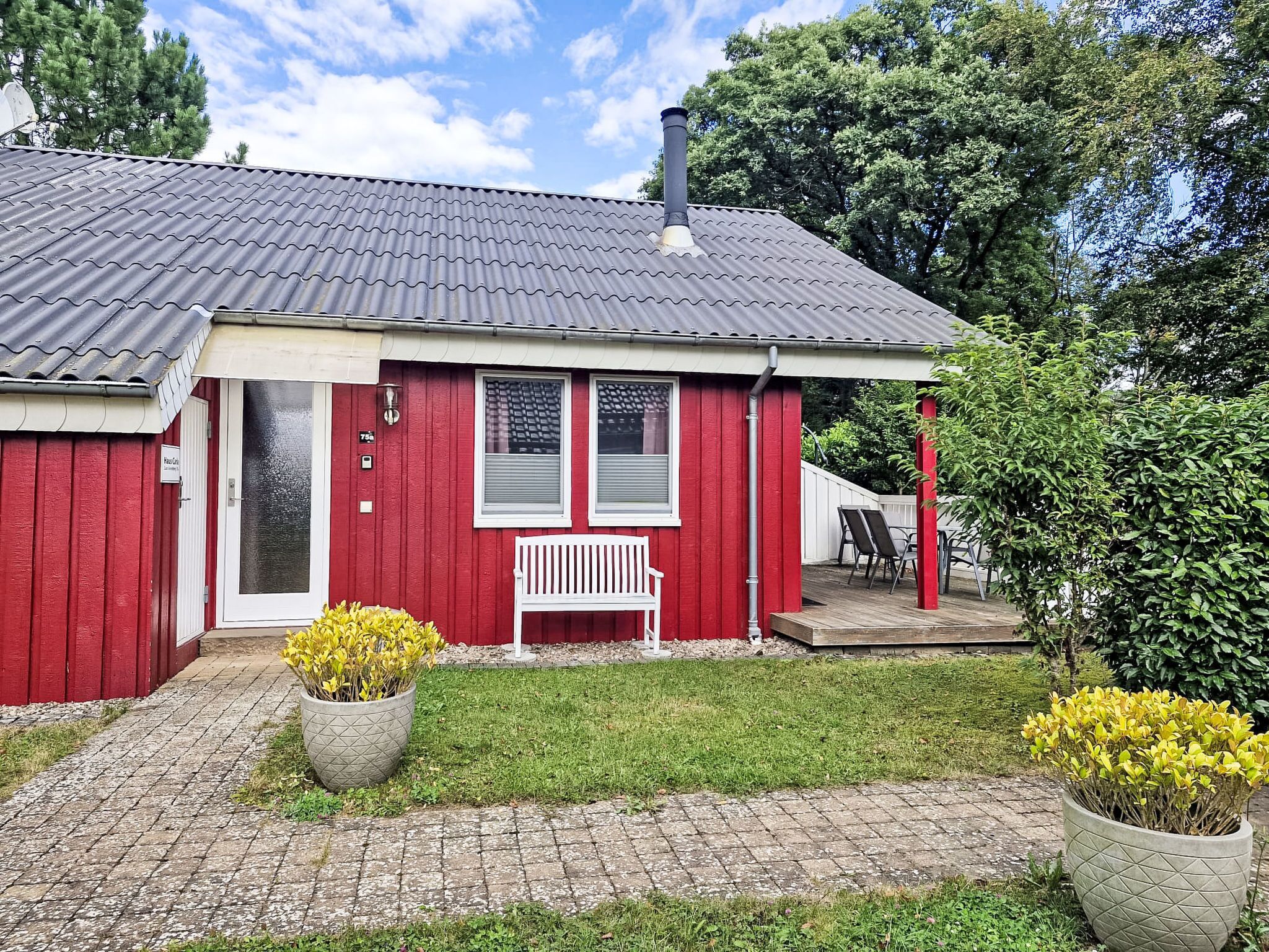 A red building with a tiled roof, a white bench, and two potted plants.