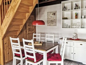Ein Essbereich mit einem Holztisch, weißen Stühlen, einer roten Pendelleuchte und einem an der Wand befestigten Regal mit Gläsern.