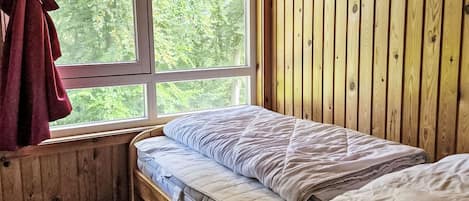 Una habitación con pared de madera, ventana con cortinas y cama con colchón y almohadas.