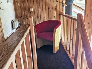 Un intérieur en bois avec une chaise rouge, un banc en bois et un petit radiateur blanc posé sur une étagère.