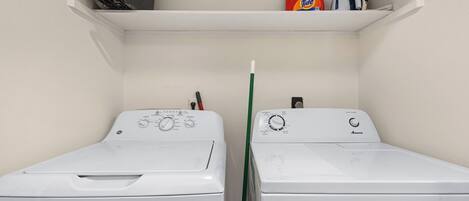 Een wasserette met twee witte wasmachines, een rode en blauwe fles wasmiddel, en een witte spuitfles op een plank.