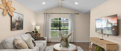 A living room with a ceiling fan, a sofa, a coffee table, a TV, and a window with curtains.