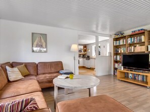 A modern living room with a sofa, coffee table, and a television. There is a bookshelf filled with books and a kitchen area in the background. - "Anina" - 300m from the sea by Interhome (Idestrup)