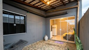 Quarto com uma grande porta de correr de vidro que dá para uma cozinha, um cilindro de gás e um banco de concreto.
