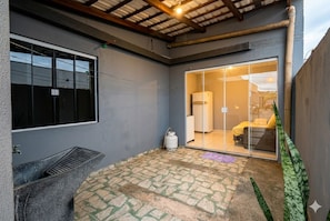 A room with a large sliding glass door leading to a kitchen area, a gas cylinder, and a concrete bench. - Studio apartment in Foz with Wi-Fi, garage, and security cameras. (Foz do Iguaçu)