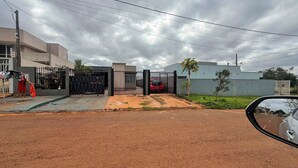 Uma área residencial com portão fechado, um carro estacionado e uma pessoa perto do portão.