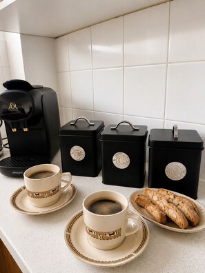 Un coin café équipé d’une machine à café, de deux tasses et d’une assiette de pain.