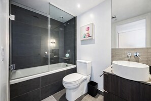 Een moderne badkamer met een douchecabine van glas, een wit toilet en een wastafelmeubel met een wastafel.