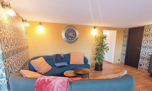 A living room with a sofa, a clock, a potted plant, and a patterned wall. - Gîtes de France® - Logis de la Mésange Bleue (GIGNAC)