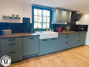 A modern kitchen with a large window, grey cabinetry, and a wooden countertop. - Gîtes de France® - Logis de la Mésange Bleue (GIGNAC)