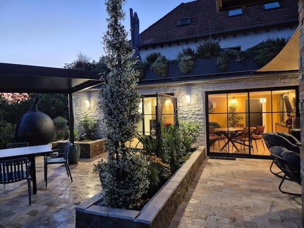 Eine Terrasse mit einer Steinsäule, einem großen Baum und Gartenmöbeln.