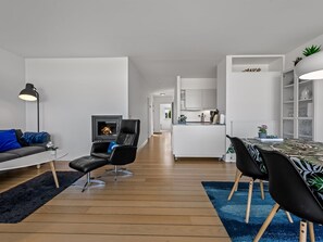 A modern living room with a fireplace, a dining area with a table and chairs, and a kitchen in the background. - "Svane" - 70m from the sea by Interhome (Ebeltoft)