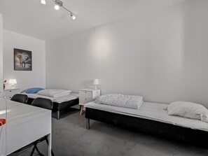 Ein modernes, minimalistisches Schlafzimmer mit zwei Einzelbetten, einem Schreibtisch und einem Stuhl.