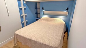 Quarto pequeno e compacto com uma cama de solteiro, prateleira embutida e escada para armazenamento.