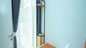 A bedroom with a bed, a wooden headboard, a nightstand, a mirror, and a window with curtains. - Cozzy Villa Dewata (batu)