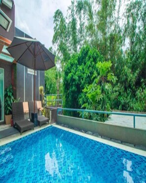 A swimming pool with lounge chairs and an umbrella, surrounded by greenery.
