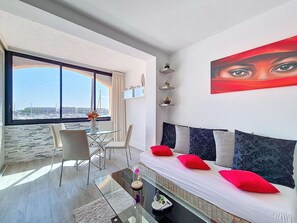 Ein modernes Wohnzimmer mit einem Glastisch, einem weißen Sofa mit roten Kissen und einem großen Fenster mit Blick auf einen Yachthafen.