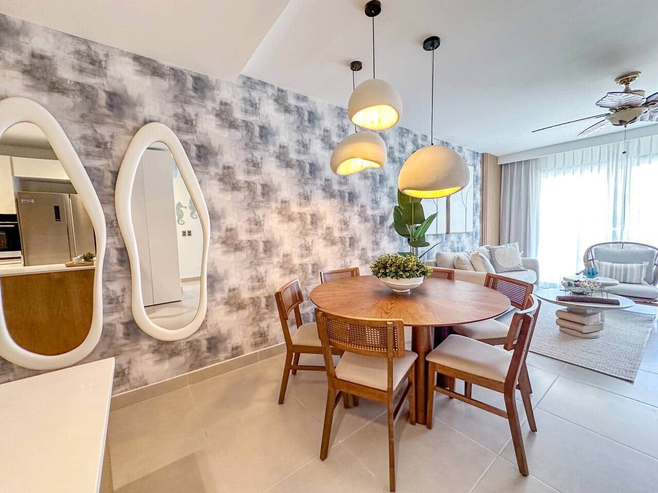 Un espace de salle à manger moderne avec une table ronde en bois, des chaises et des luminaires suspendus.