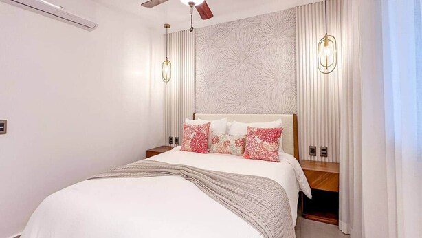 Een slaapkamer met een bed, nachtkastjes, een plafondventilator en een behang met een patroon.