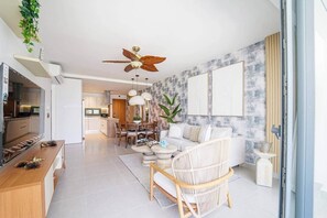 Ein modernes Wohnzimmer mit einer Couch, einem Essbereich und einer durchgehenden Tür erkennbaren Küche.