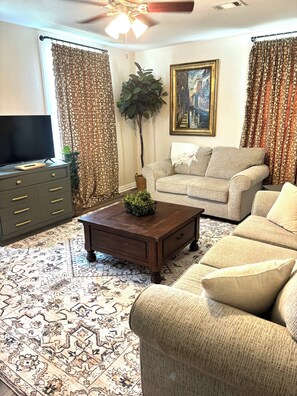 A living room with a sofa, a coffee table, a television, and a plant.
