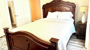 Ein ordentlich bezogenes Bett mit einem Holz-Kopfteil, weißer Bettwäsche und einem Nachttisch mit Lampe.