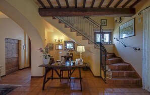 Una escalera con barandilla de hierro forjado que lleva a un rellano con una mesa y sillas, una puerta de madera y una pared con un cuadro enmarcado.