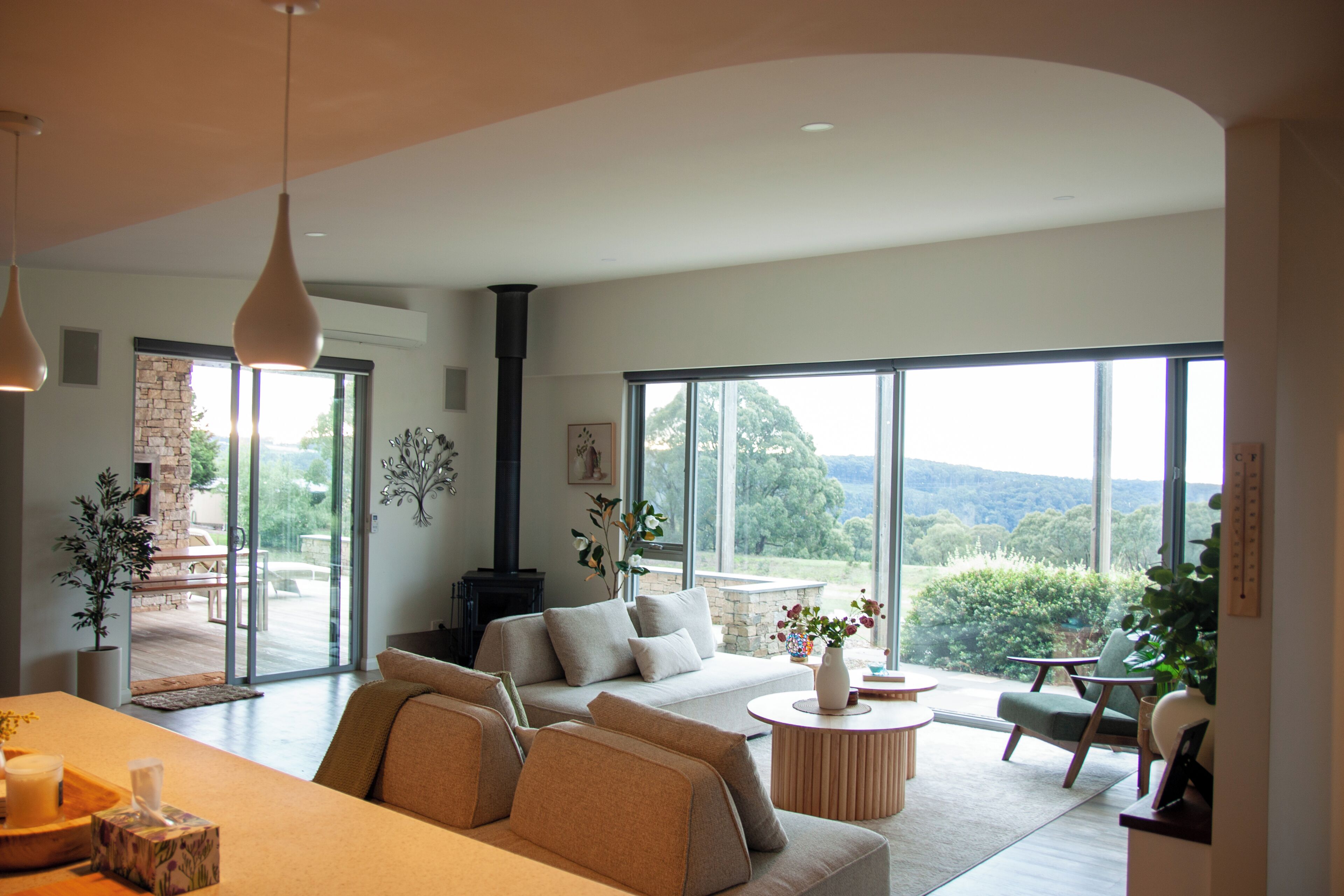 Un salon spacieux comprenant un ensemble de canapés, une table basse et une cheminée. De grandes fenêtres offrent une vue sur l’extérieur.