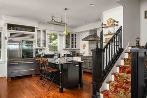 Een ruime keuken met een centraal eiland, een eethoek met stoelen, en een trap met decoratieve balustrades.
