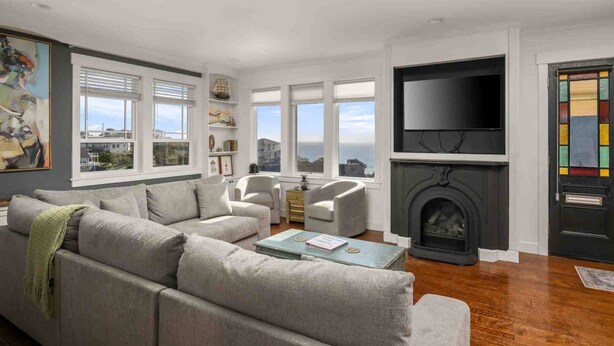 A living room with a sofa, chairs, a fireplace, a TV, and a view of the sea through large windows. - Ocean Views, Hot Tub, Fireplaces & Luxury Finishes, Chef's Kitchen, Community Pool, EV Charger, BBQ (Lincoln City)