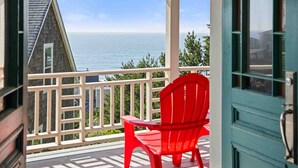 A balcony with a red chair and table, overlooking a body of water and a building. - Ocean Views, Hot Tub, Fireplaces & Luxury Finishes, Chef's Kitchen, Community Pool, EV Charger, BBQ (Lincoln City)
