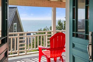 A balcony with a red chair and table, overlooking a body of water and a building. - Ocean Views, Hot Tub, Fireplaces & Luxury Finishes, Chef's Kitchen, Community Pool, EV Charger, BBQ (Lincoln City)