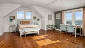 A bedroom with a bed, bedside tables, a desk, and a chair. There are windows and a view of the sea. - Ocean Views, Hot Tub, Fireplaces & Luxury Finishes, Chef's Kitchen, Community Pool, EV Charger, BBQ (Lincoln City)
