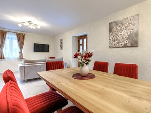 Ein modernes Wohnzimmer mit Esstisch, roten Polsterstühlen, einem Flachbildfernseher und einem floralen Kunstwerk an der Wand.