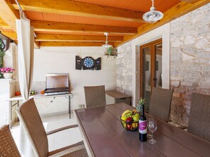 A wooden ceiling, a stone wall, a dining table with chairs, a grill, and a dartboard. - Vacation home Trošti by Interhome (Barban)