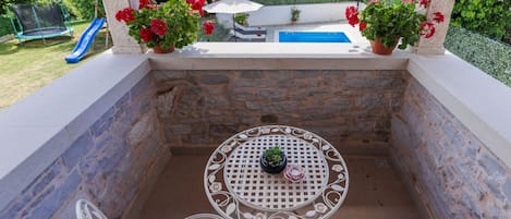 A covered outdoor seating area with stone walls, a pool, and potted plants.