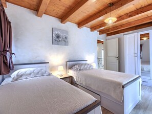 Ein Schlafzimmer mit zwei Betten, Holzbalken an der Decke, einer weißen Wand mit einem Löwenzahn-Kunstwerk und einer Tür zu einem anderen Raum.