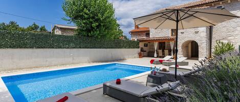 A swimming pool with lounge chairs and an umbrella, surrounded by stone walls and vegetation.