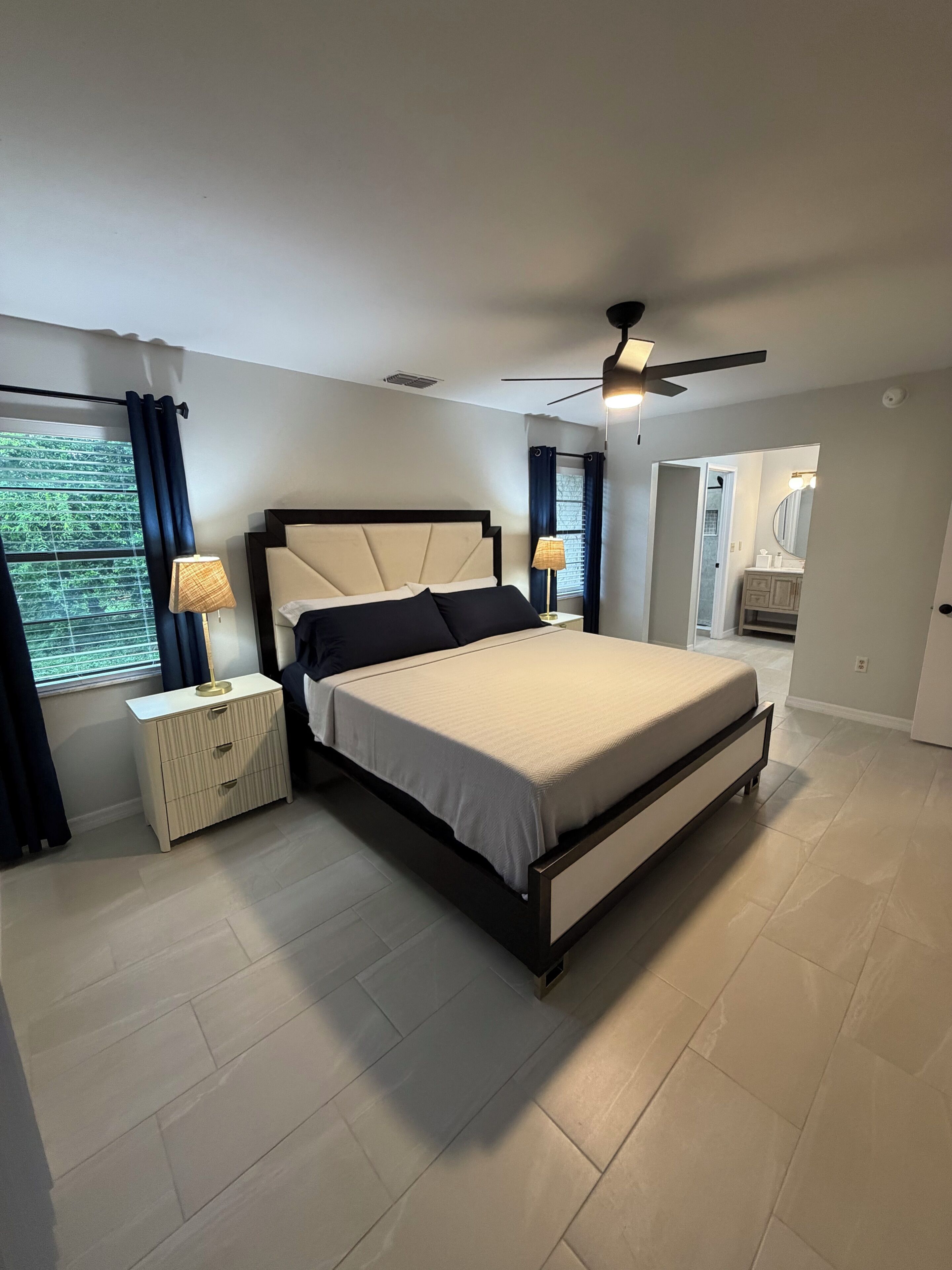 A bedroom with a bed, nightstands, a ceiling fan, and a view of the bathroom.