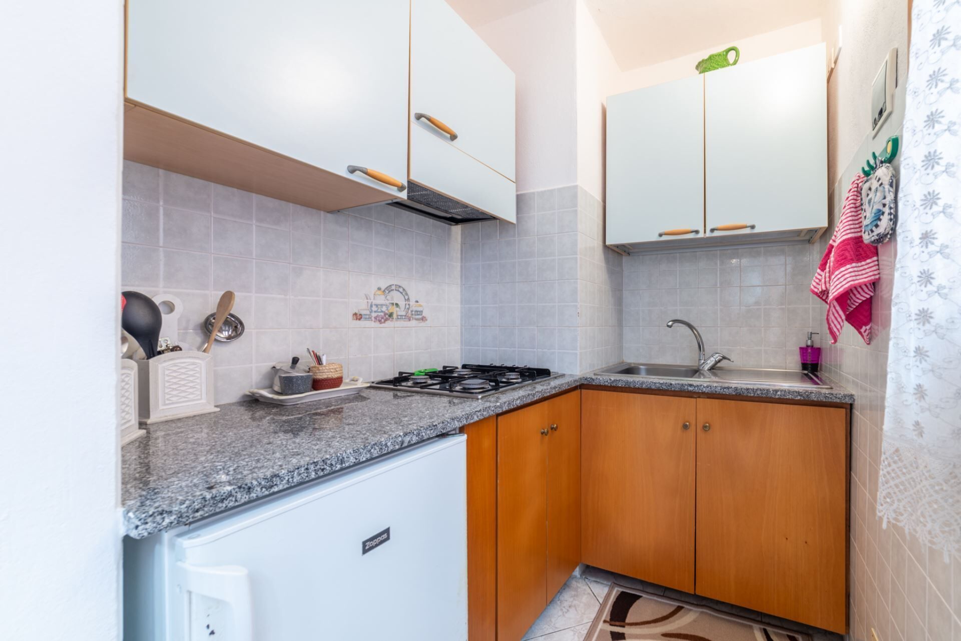 Una cucina compatta con fornello, lavello e mobili impiallacciati in legno.
