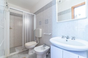 Ein Badezimmer mit Dusche, Toilette, Bidet, Waschbecken und Spiegel.