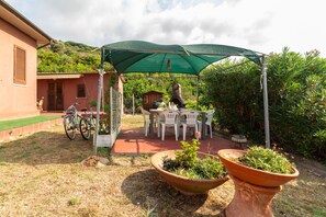 Eine Terrassenanlage mit Tisch, Stühlen, einem grünen Sonnenschirm und Blumentöpfen.
