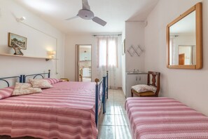 Ein Schlafzimmer mit zwei Betten, einem Deckenventilator, einem Spiegel und Blick in den angrenzenden Raum.